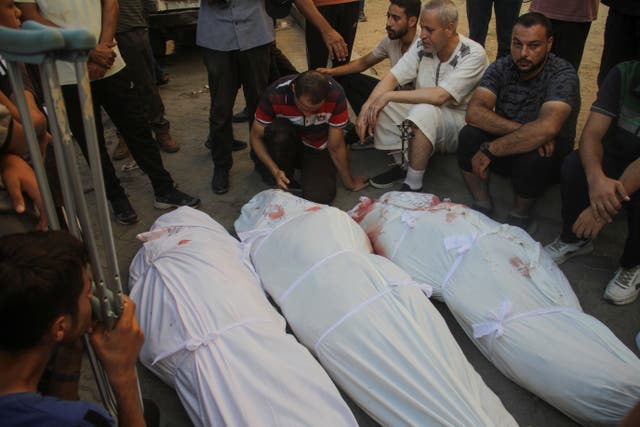 <p>Mourners sit next to bodies recovered over the weekend in a school and compound in Gaza where refugees were sheltering from Israeli strikes. Israeli officials say just over a dozen militants were killed in the attack</p>