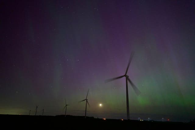 <p>Windmills turn in a field near London, Ontario as the Northern lights or aurora borealis illuminate the night sky during a geomagnetic storm on May 10, 2024</p>